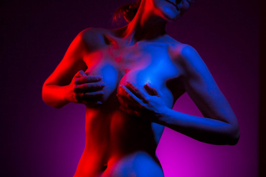 Aktfoto des Körpers einer Frau die Ihre Brüste mit den Händen bedeckt in rotem und blauem Licht