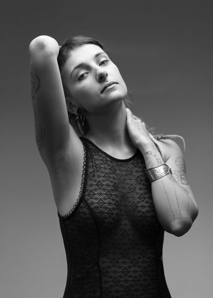 Schwarzweiß Portraitfoto einer Frau mit Tattoos und Nasenpiercing in einem Body aus schwarzer Spitze